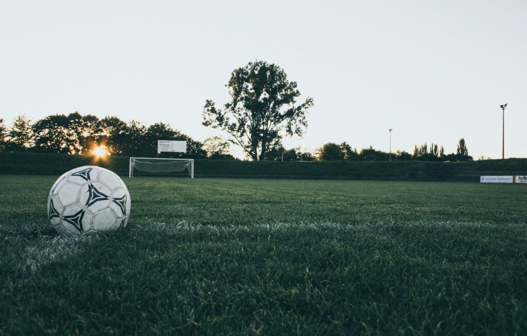 pexels-photo-114296 Soccer ball on field at sunrise, serene landscape with goalpost in background.