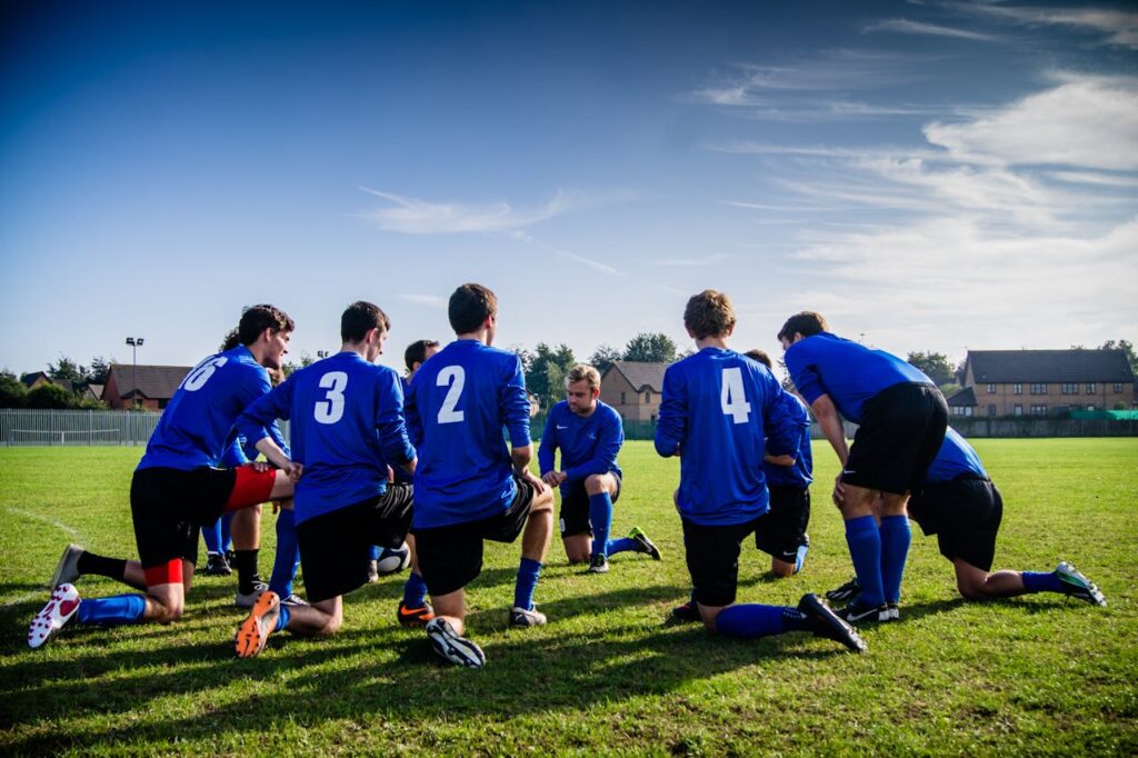 pexels-photo-262524 A group of male football players in blue uniforms huddle on a grassy field before a match.